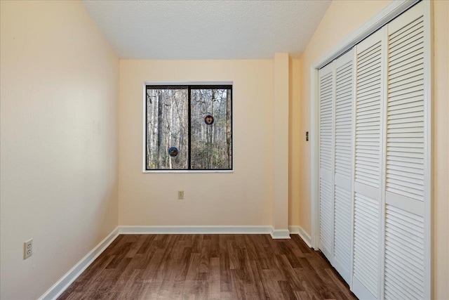 unfurnished bedroom with a textured ceiling, a closet, dark wood finished floors, and baseboards