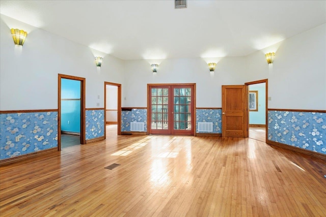 unfurnished room with a wainscoted wall, french doors, light wood finished floors, and wallpapered walls