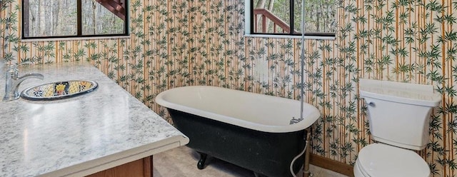 bathroom with a soaking tub, toilet, and wallpapered walls