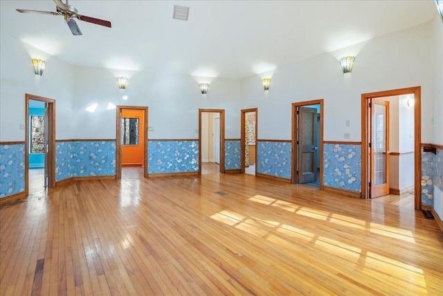 spare room with ceiling fan, visible vents, light wood-type flooring, wainscoting, and wallpapered walls