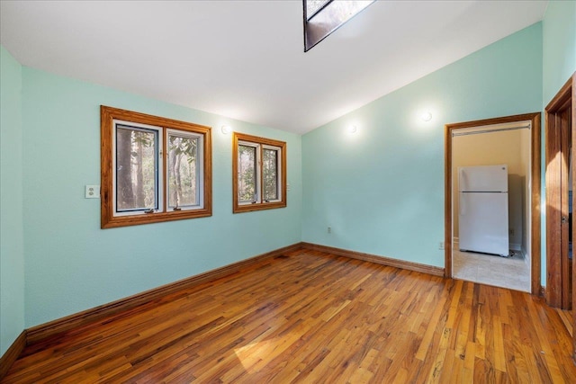 spare room featuring light wood-style floors, vaulted ceiling, and baseboards