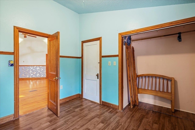 unfurnished bedroom with a textured ceiling, baseboards, and wood finished floors