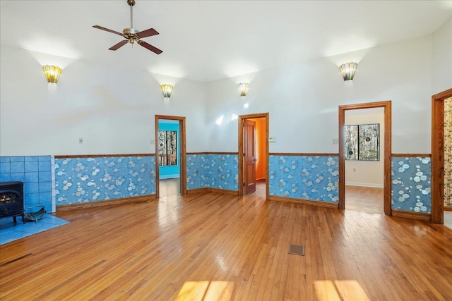 unfurnished living room featuring a wood stove, a wainscoted wall, wallpapered walls, and wood finished floors