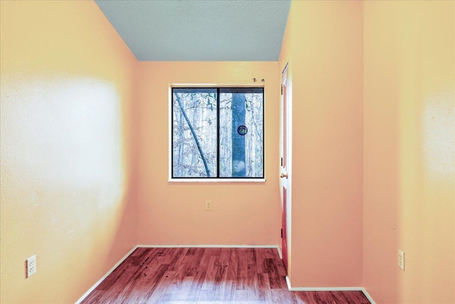 spare room featuring a textured ceiling, wood finished floors, and baseboards