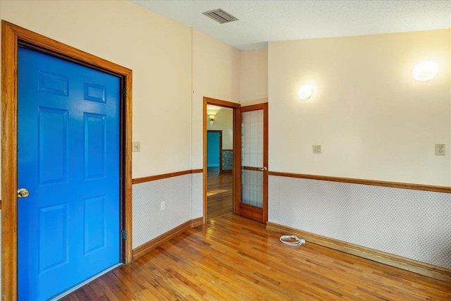 entryway with a wainscoted wall, visible vents, wallpapered walls, and wood finished floors