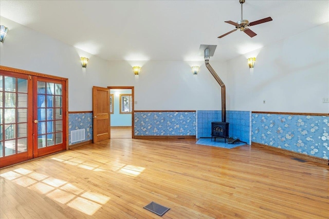 spare room featuring a wainscoted wall, visible vents, french doors, light wood-type flooring, and a wood stove