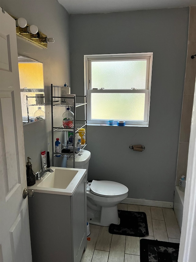 bathroom with a tub to relax in, hardwood / wood-style floors, vanity, and toilet