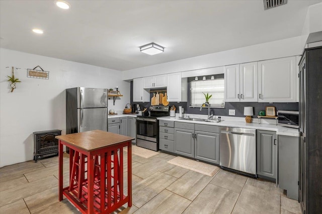 kitchen with sink, appliances with stainless steel finishes, gray cabinetry, white cabinets, and a wood stove