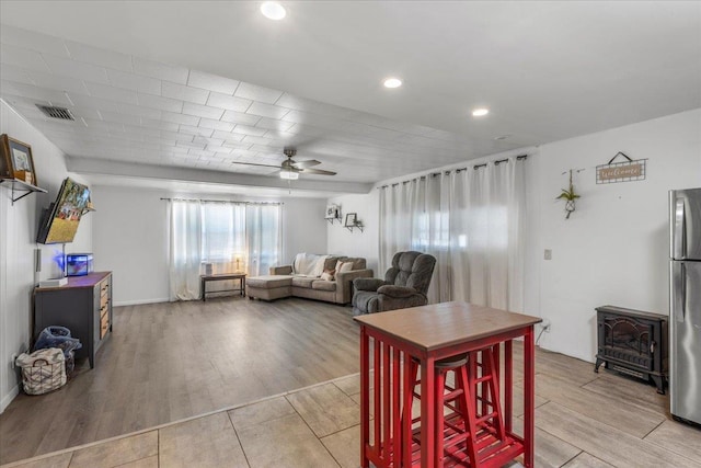 living room with ceiling fan, a wood stove, and light hardwood / wood-style floors