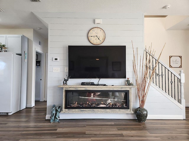 interior space featuring dark wood-type flooring, a glass covered fireplace, visible vents, and stairs