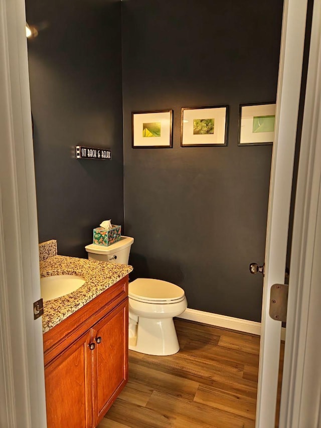 half bathroom featuring toilet, baseboards, wood finished floors, and vanity