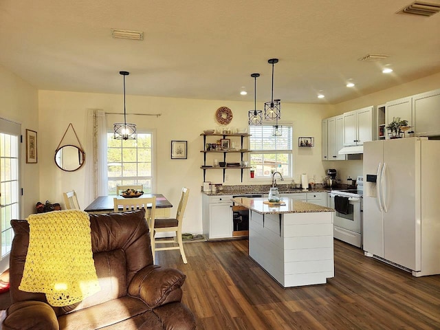 kitchen featuring white appliances, dark wood-type flooring, visible vents, a wealth of natural light, and a center island