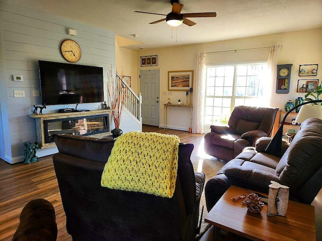 living room featuring ceiling fan, a textured ceiling, stairway, and wood finished floors