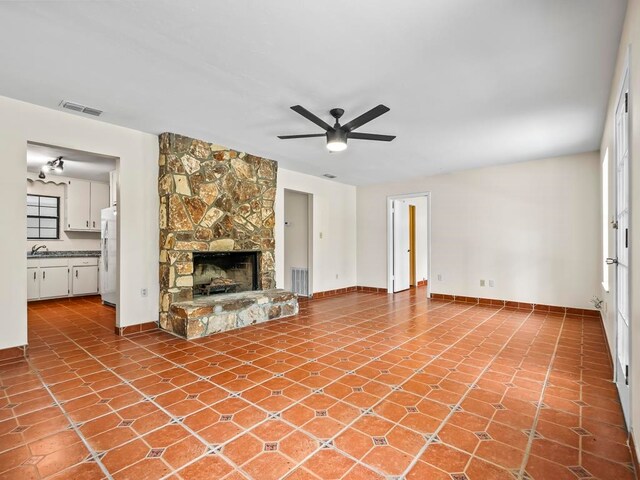 unfurnished living room with a stone fireplace, sink, light tile patterned floors, and ceiling fan