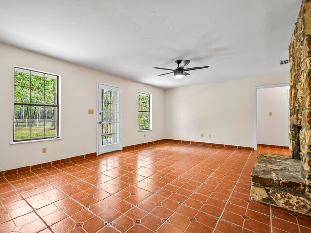 tiled empty room featuring a fireplace and ceiling fan