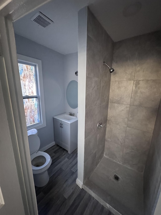 bathroom with hardwood / wood-style flooring, vanity, tiled shower, and toilet