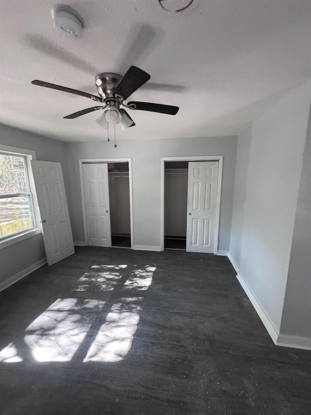 unfurnished bedroom featuring ceiling fan, multiple closets, and a textured ceiling