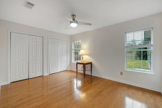 unfurnished bedroom with multiple closets, ceiling fan, and light wood-type flooring