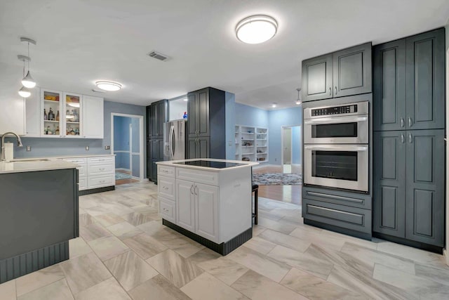 kitchen featuring sink, appliances with stainless steel finishes, a center island, white cabinets, and decorative light fixtures