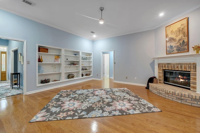 living area featuring ceiling fan, a brick fireplace, crown molding, and light wood-type flooring