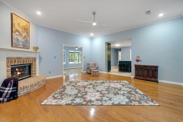 living room featuring ceiling fan, ornamental molding, wood-type flooring, and a brick fireplace