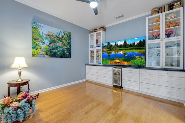 living room featuring wine cooler, ornamental molding, bar, ceiling fan, and light hardwood / wood-style floors