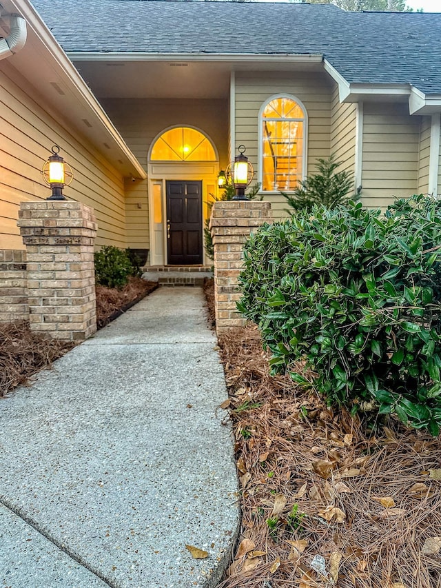 doorway to property with a porch and a shingled roof