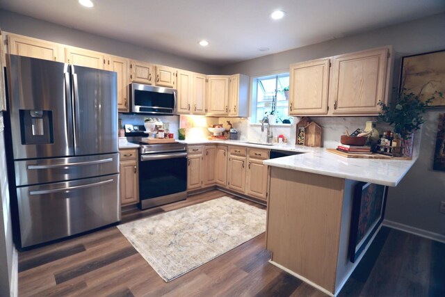 kitchen with light brown cabinetry, recessed lighting, appliances with stainless steel finishes, a peninsula, and a sink