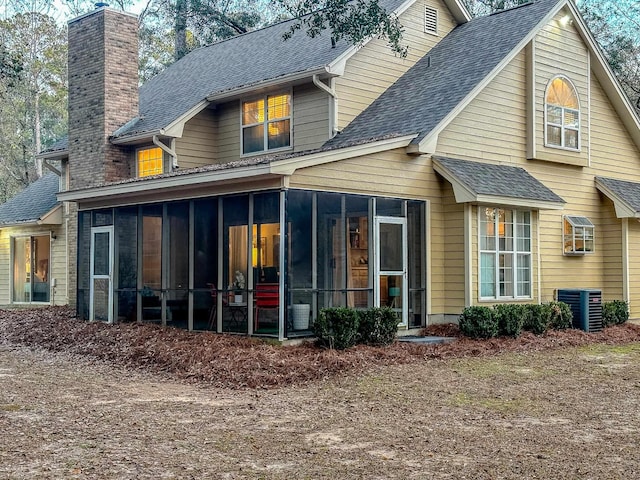 back of property featuring central air condition unit, a sunroom, a chimney, and a shingled roof