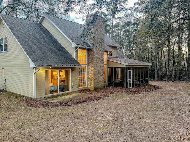 back of property featuring roof with shingles, a sunroom, and a chimney