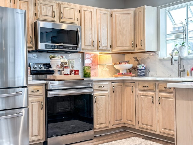 kitchen with light brown cabinets, a sink, decorative backsplash, light countertops, and appliances with stainless steel finishes