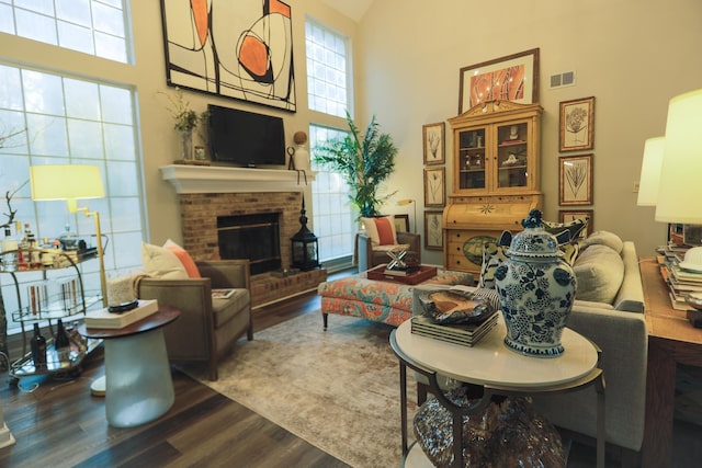 living area featuring visible vents, a high ceiling, a brick fireplace, and wood finished floors