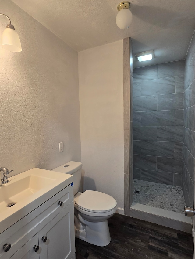 bathroom featuring tiled shower, wood-type flooring, toilet, a textured ceiling, and vanity