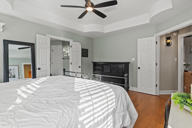 bedroom with a raised ceiling, wood-type flooring, and ceiling fan