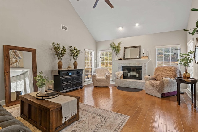 living room with plenty of natural light, high vaulted ceiling, a brick fireplace, and light wood-type flooring