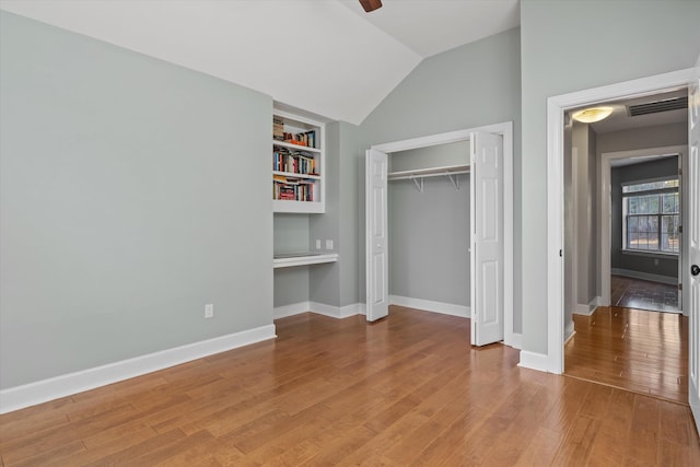 unfurnished bedroom featuring built in desk, wood-type flooring, lofted ceiling, ceiling fan, and a closet