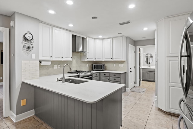 kitchen with wall chimney exhaust hood, gray cabinetry, white cabinetry, appliances with stainless steel finishes, and kitchen peninsula