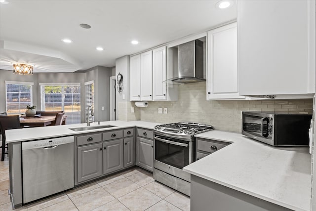 kitchen with sink, gray cabinetry, stainless steel appliances, kitchen peninsula, and wall chimney exhaust hood