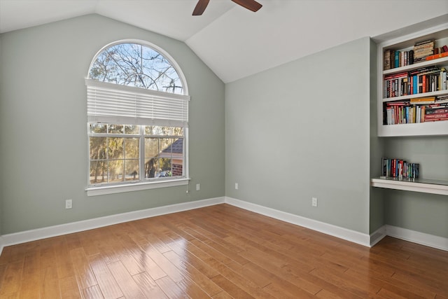 unfurnished room featuring built in shelves, wood-type flooring, built in desk, vaulted ceiling, and ceiling fan