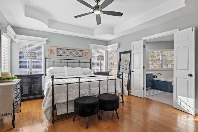 bedroom featuring ensuite bath, a raised ceiling, and light hardwood / wood-style flooring