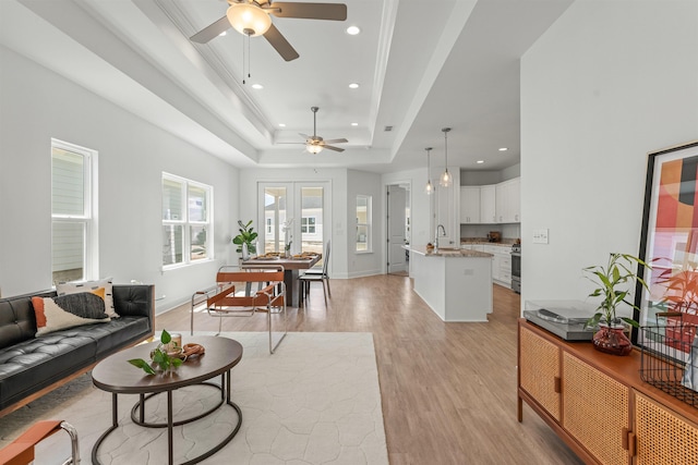 living room featuring ceiling fan, sink, french doors, a tray ceiling, and light wood-type flooring