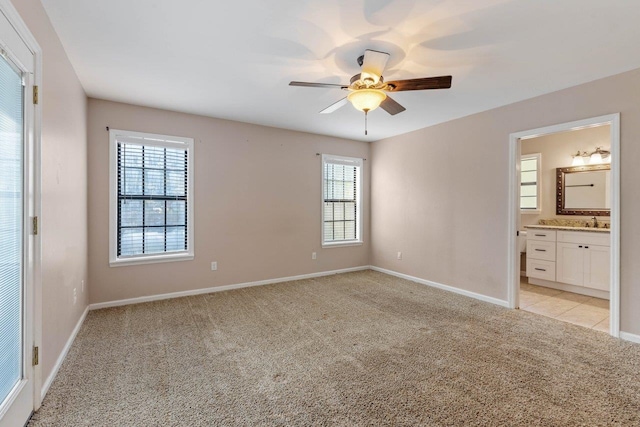 unfurnished bedroom with multiple windows, light carpet, ceiling fan, and ensuite bathroom