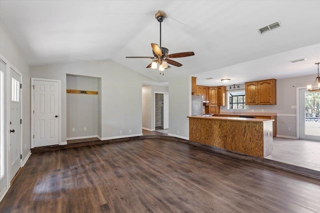 interior space featuring vaulted ceiling, kitchen peninsula, dark hardwood / wood-style floors, ceiling fan, and stainless steel refrigerator