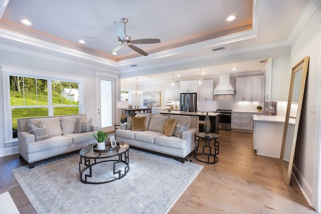 living room with ceiling fan, a raised ceiling, light wood-type flooring, and ornamental molding