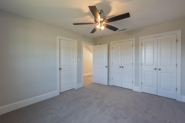 unfurnished bedroom featuring ceiling fan, multiple closets, and light colored carpet