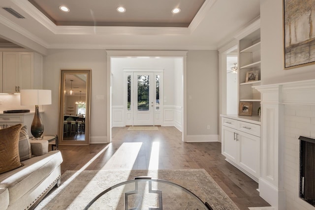 entryway with a brick fireplace, dark wood-type flooring, ornamental molding, ceiling fan, and a tray ceiling