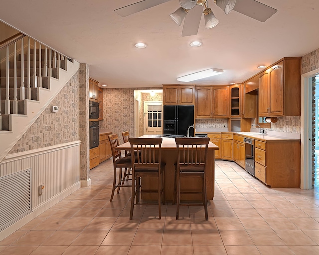 kitchen with black appliances, light tile patterned floors, sink, a kitchen island, and a breakfast bar