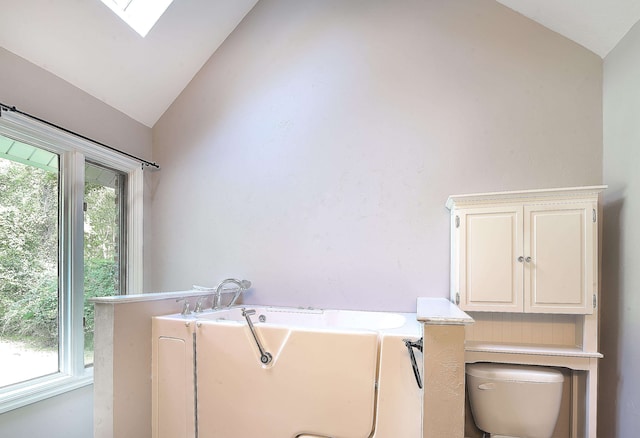 bathroom featuring lofted ceiling with skylight, a bath, and toilet