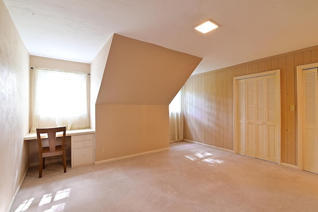 additional living space with light colored carpet, wood walls, built in desk, and vaulted ceiling