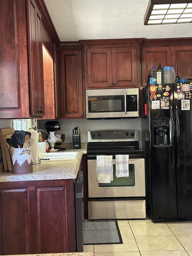 kitchen with light tile patterned floors, stainless steel appliances, a textured ceiling, light countertops, and a sink